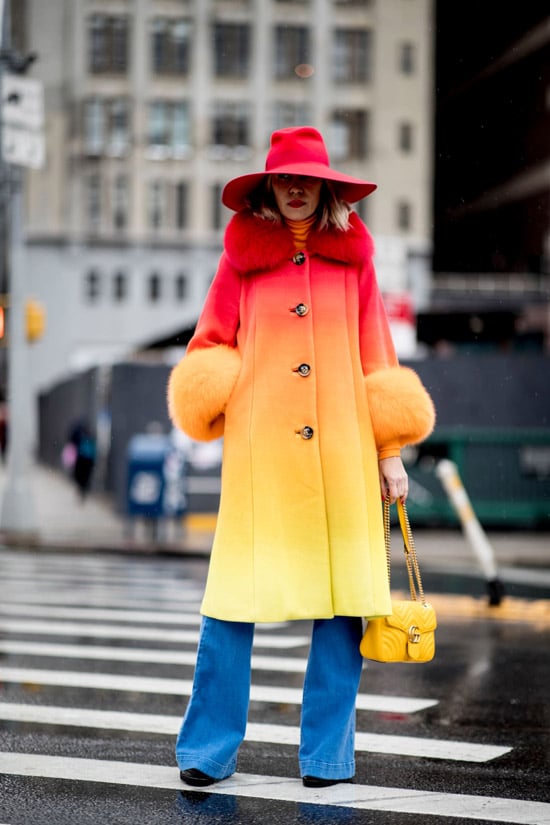 Девушка в красно-желтом пальто омбре, синие джинсы и красная шляпа
